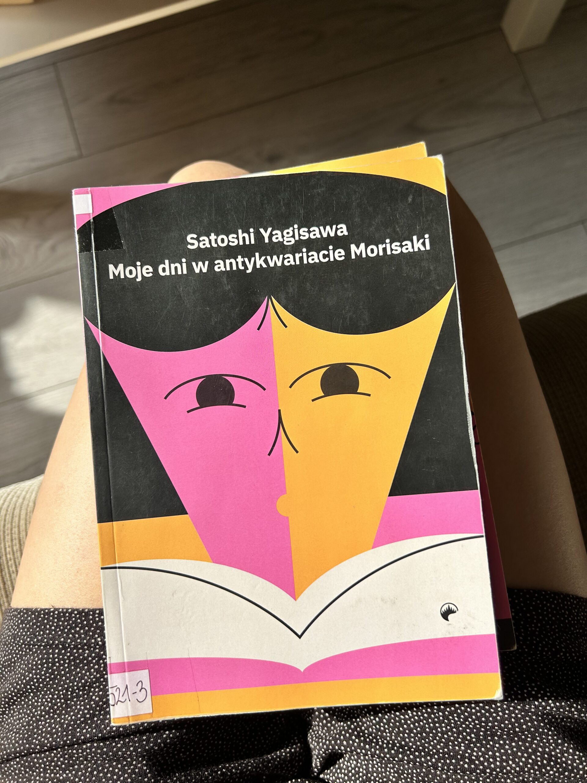 Kolorowa fotografia. Książka leży na kolanach. W tle drewniana podłoga.