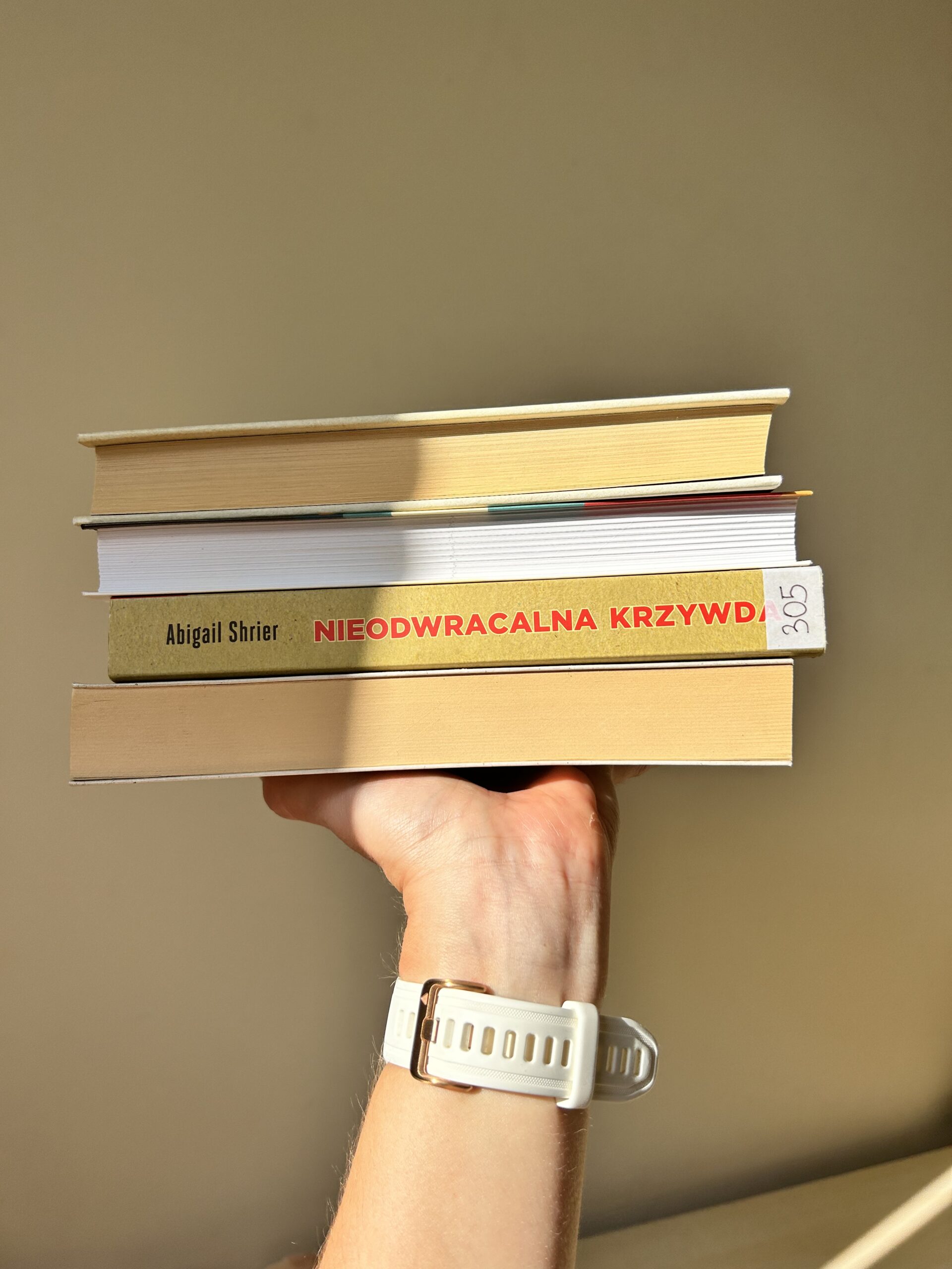 Kolorowe zdjęcie. Wyciągnięta ręka trzyma stos książek. Na nadgarstku zegarek z białym paskiem.