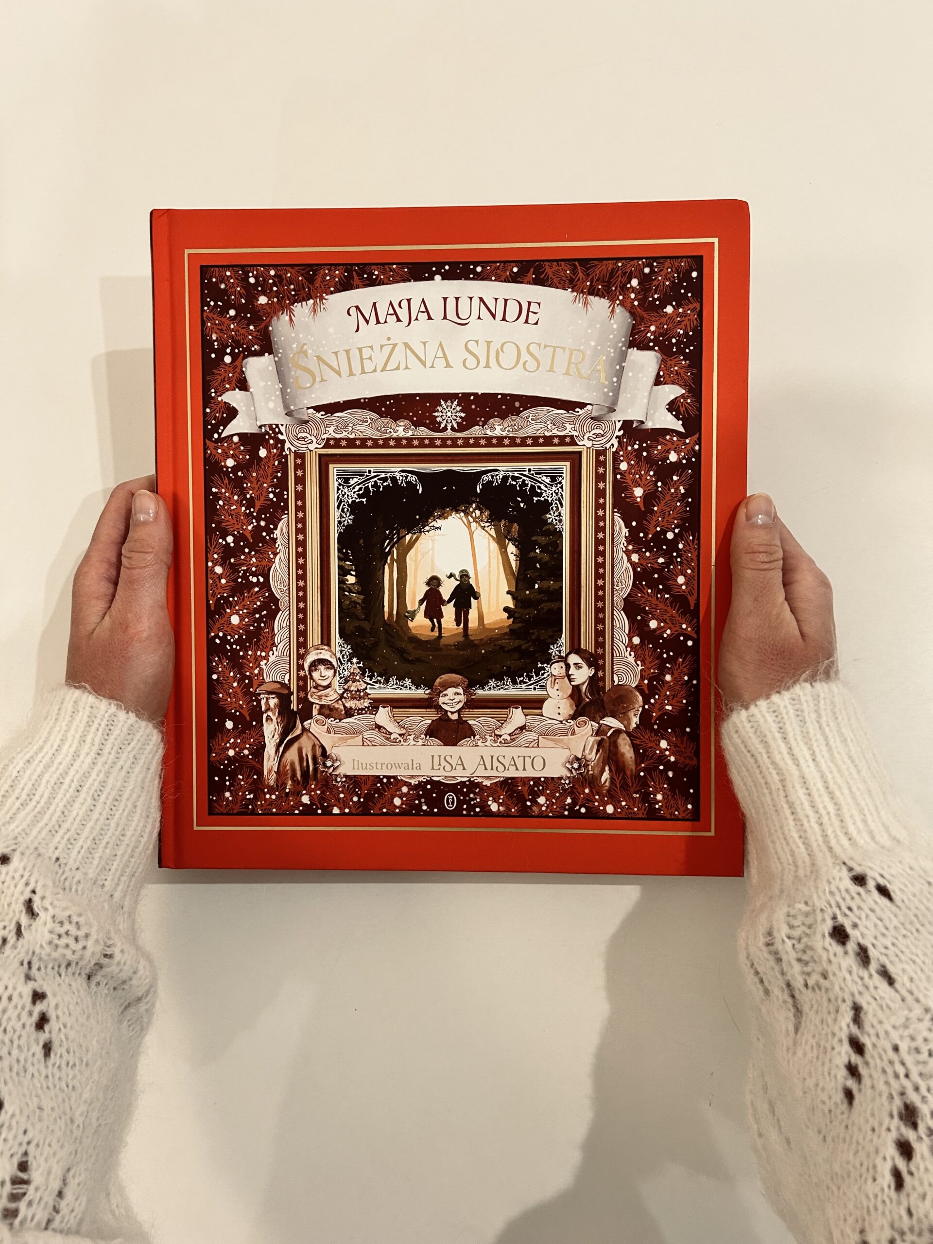 Kolorowe zdjęcie. Wyciągnięte ręce trzymają książkę. W tle biały blat stołu.