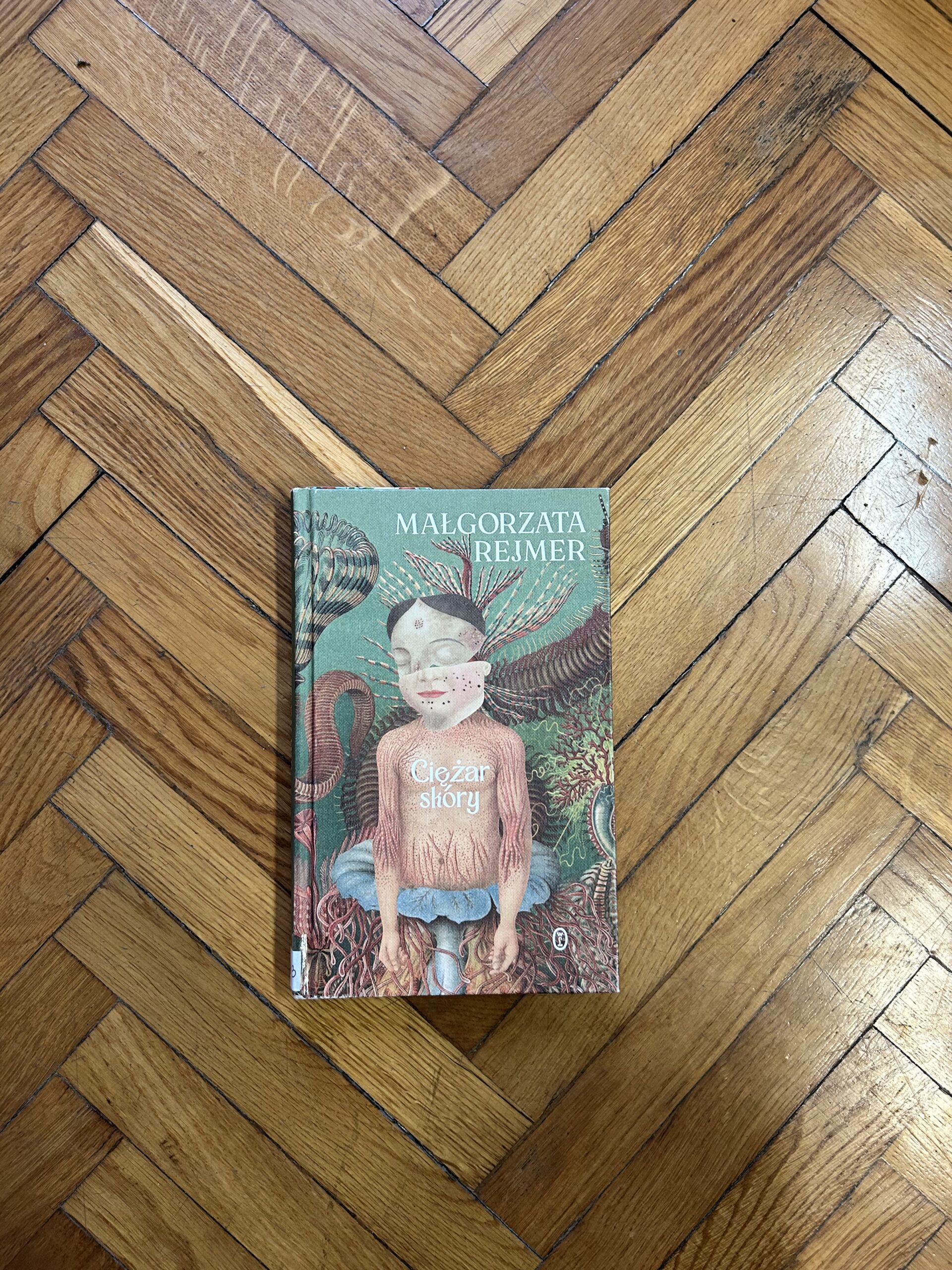 Kolorowe zdjęcie. Zamknięta książka leży na drewnianym parkiecie.