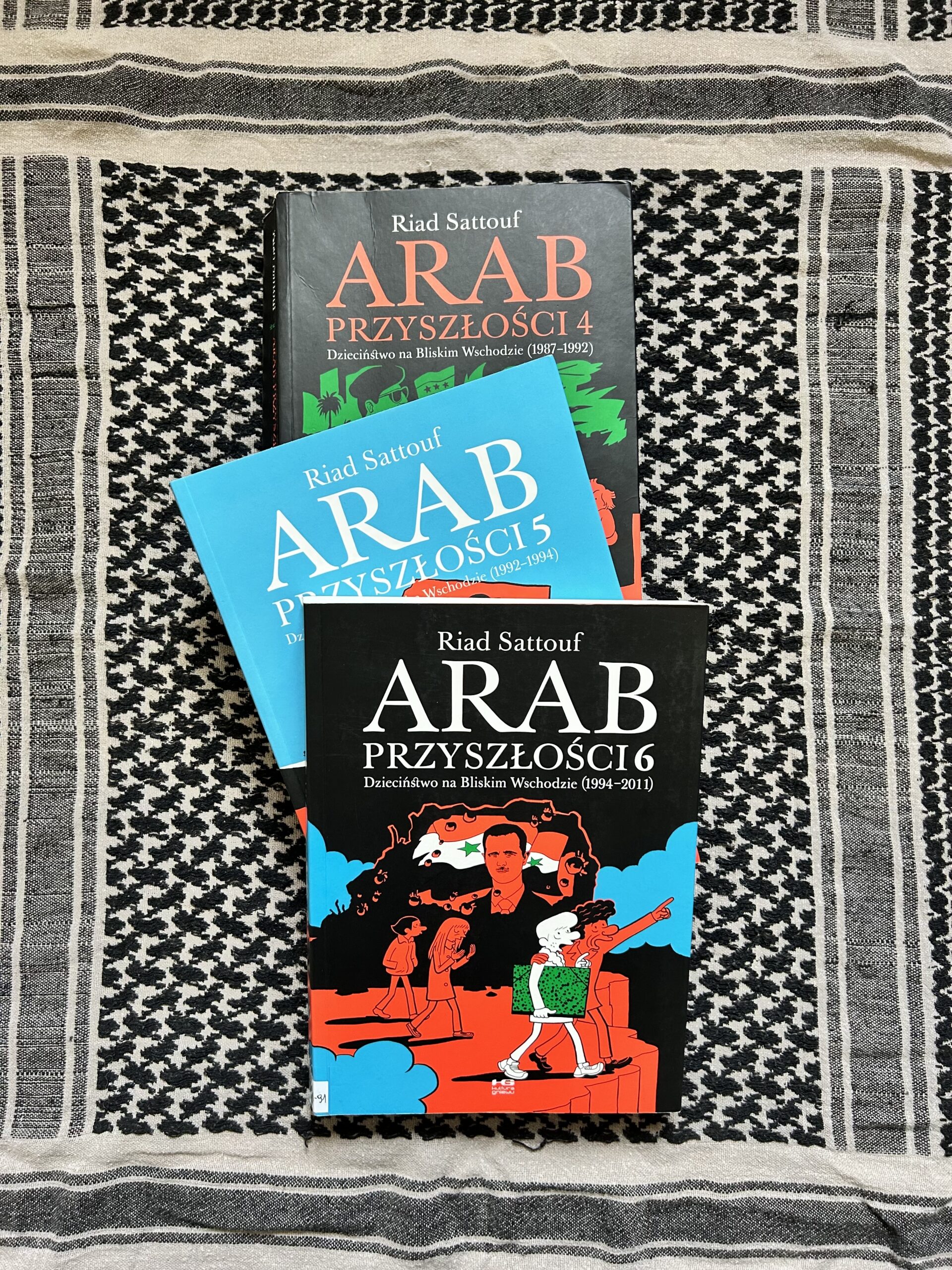 Kolorowe zdjęcie. 3 książki leżą na sobie. Pod nimi chusta arabska.