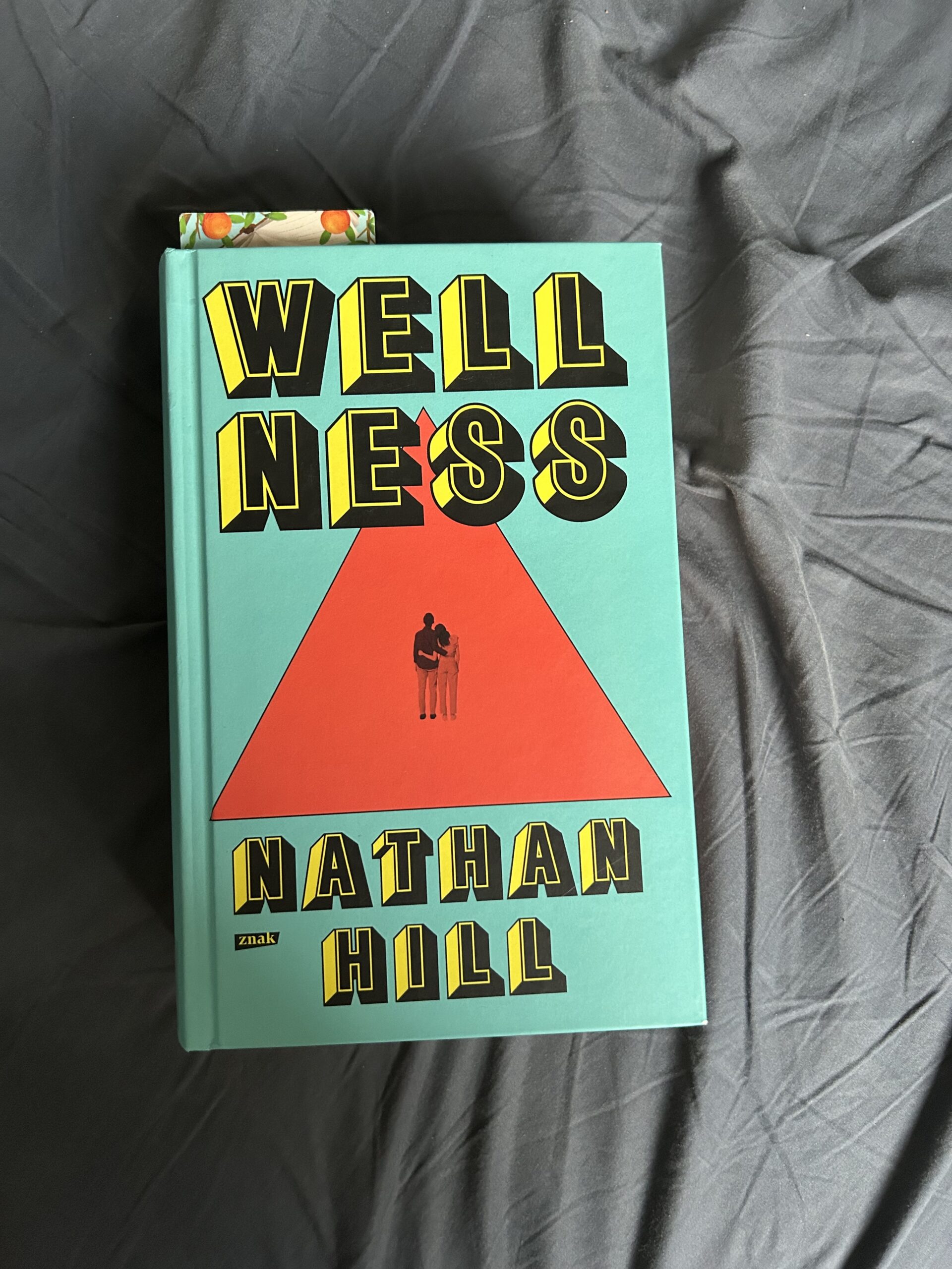 Kolorowe zdjęcie. Zamknięta książka leży na pomiętym prześcieradle.